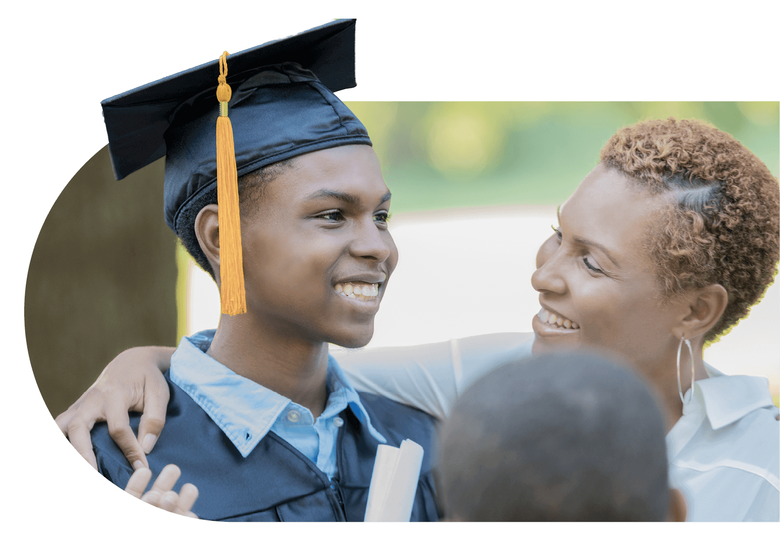 student in cap and gown smiles, holding dimploma while proud mother smiles back